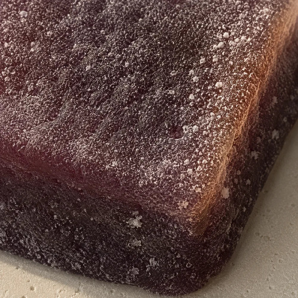 A single deep plum gummy cube filling the frame, matte and lightly dusted