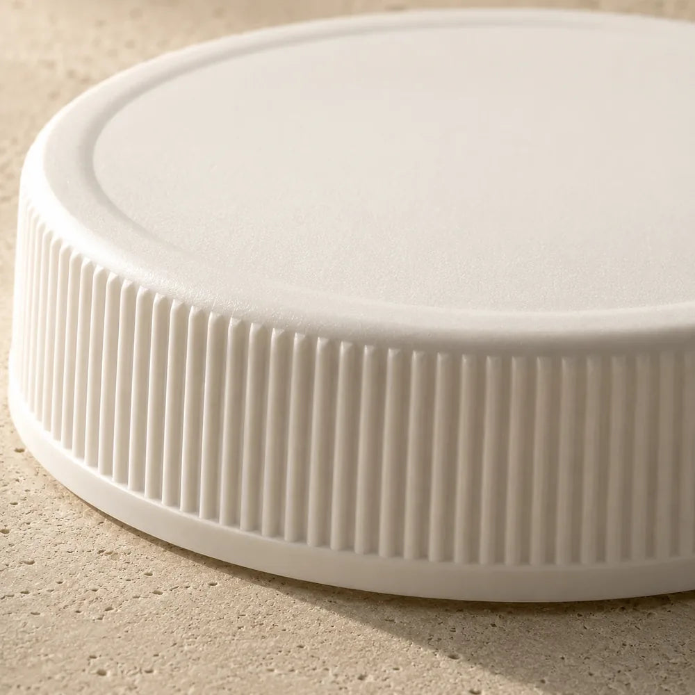 A matte white ribbed screw cap lying on pale limestone