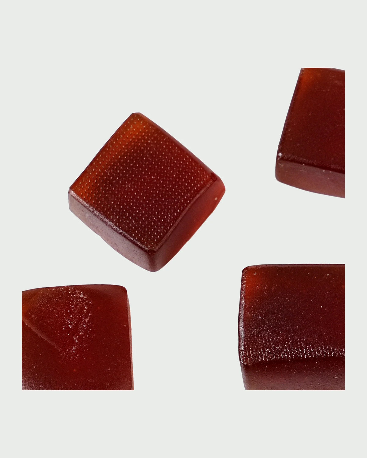 Four Veya gummies at close range: deep red pectin cubes with a fine moulded texture on the top face.